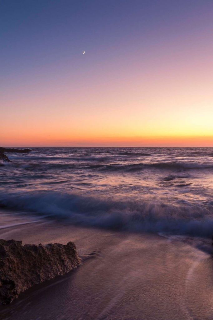 Światło księżyca nad fioletowymi falami o zachodzie słońca.