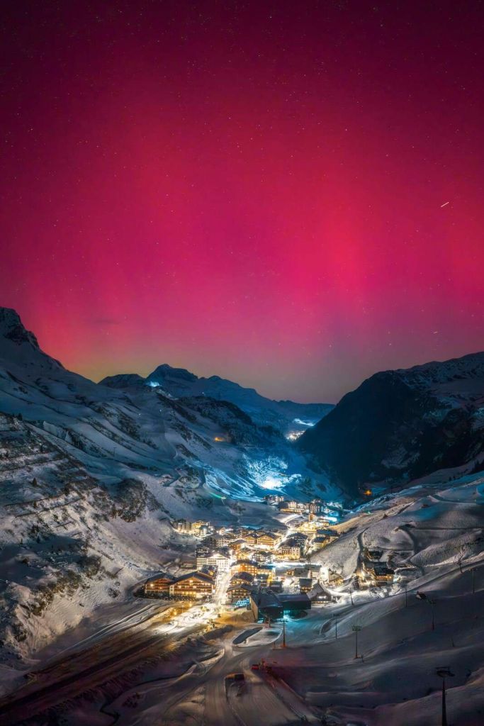 R√≥≈ºowa zorza polarna nad g√≥rskƒÖ wioskƒÖ