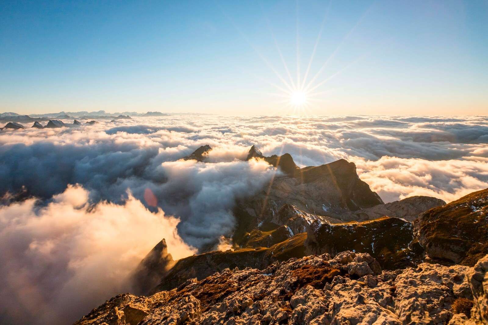 Słońce nad chmurami i szczytami gór.