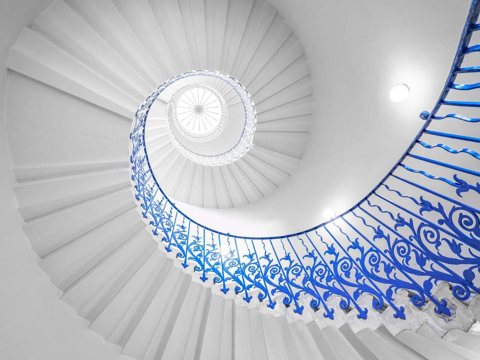 Białe spiralne schody z niebieską poręczą